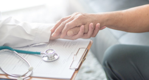 Stock photo of a doctor holding an older patient's hand against a gray background