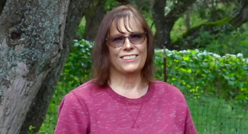 Christine, an older woman, smiles in front of trees