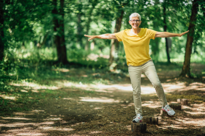 Older woman balances on log; balance can help prevent falls